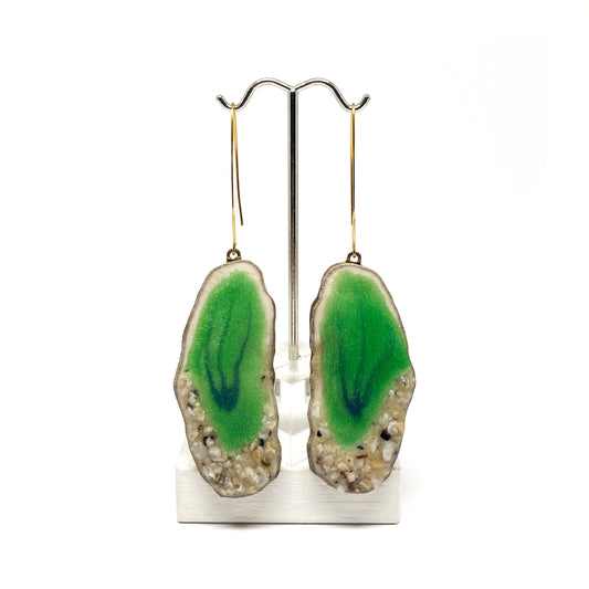 Two round earrings with green geode-like designs, displayed on a silver earring stand.