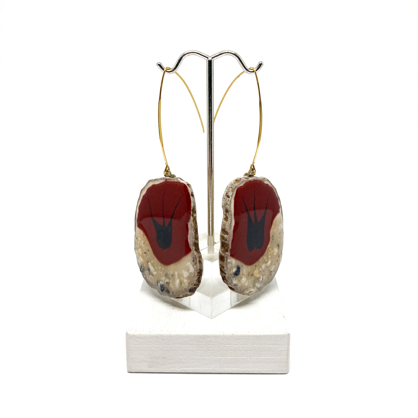 Two round earrings with red and black bird-shaped designs, displayed on a silver earring stand.