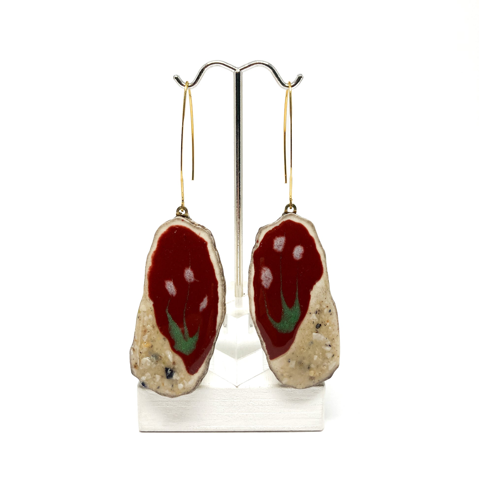 Two round earrings with red and white flower-like designs, displayed on a silver earring stand.