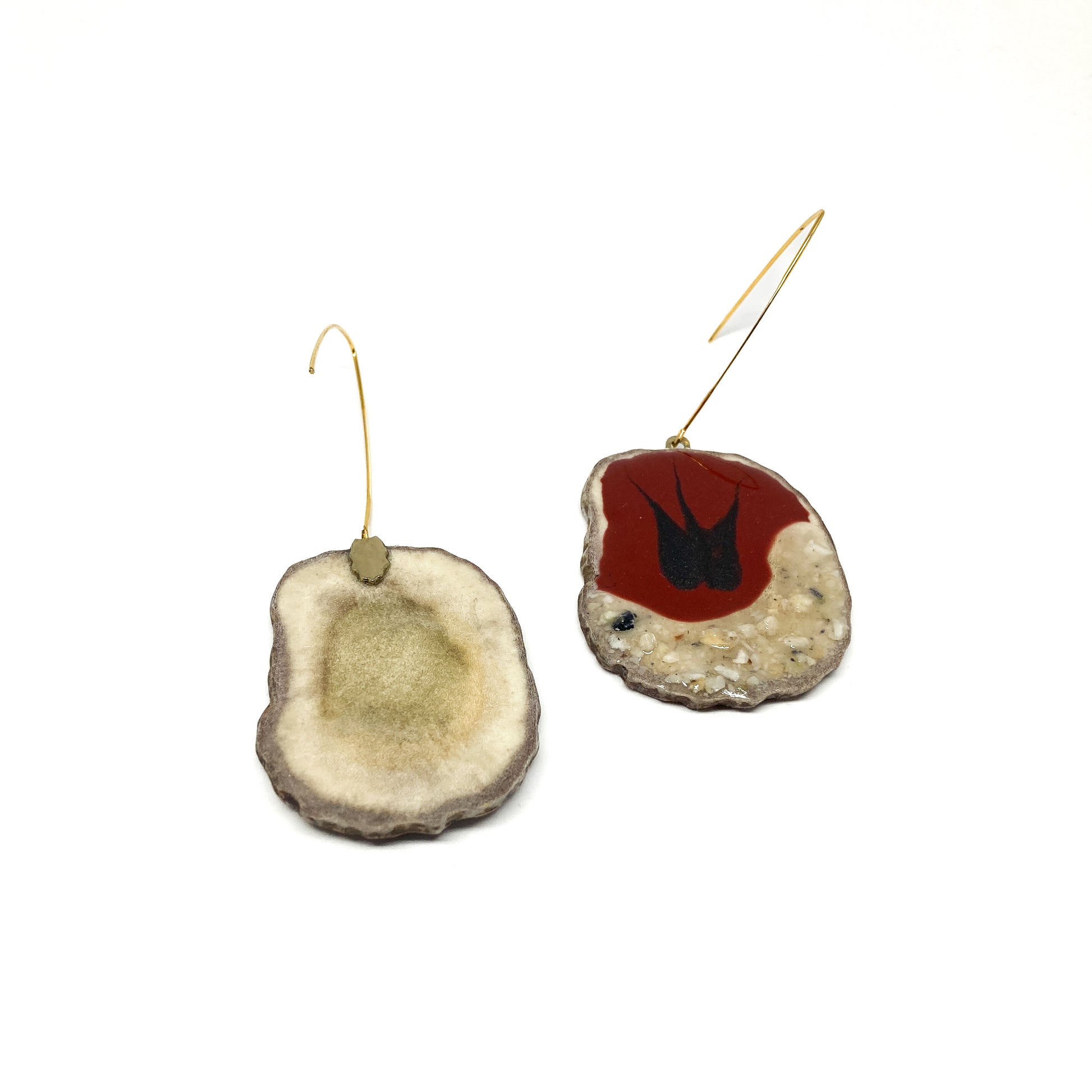 Two mismatched earrings, one with a red and black bird-shaped design, the other with a slice of antler and a gold hook.