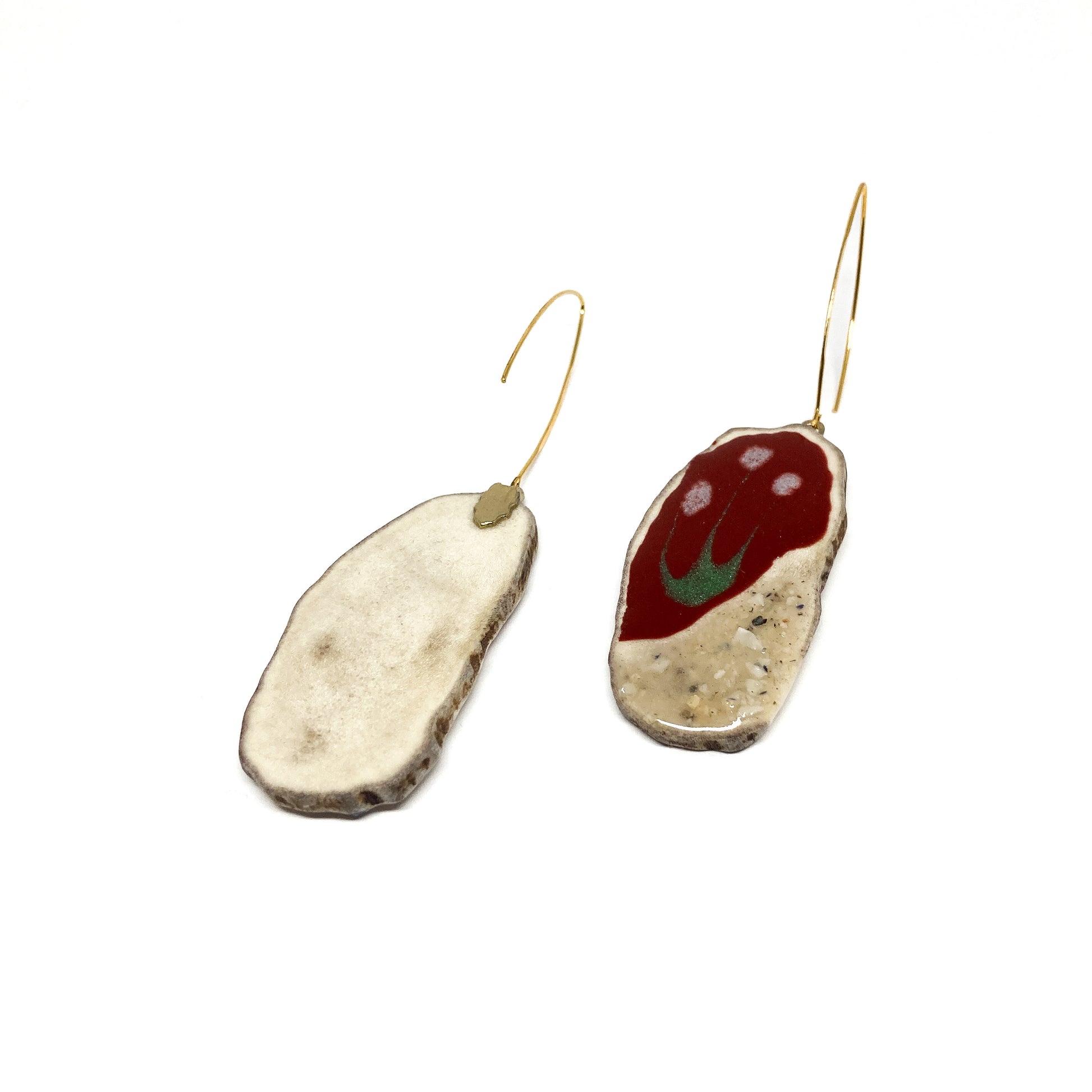 Two mismatched earrings, one with a red and white design, the other with a slice of antler and a gold hook.