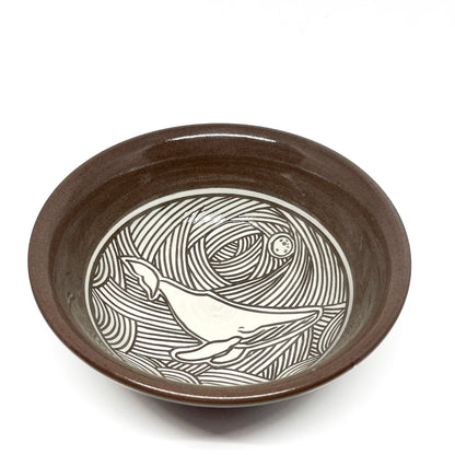 Ceramic bowl with a carved whale swimming beneath a full moon, surrounded by swirling wave patterns.