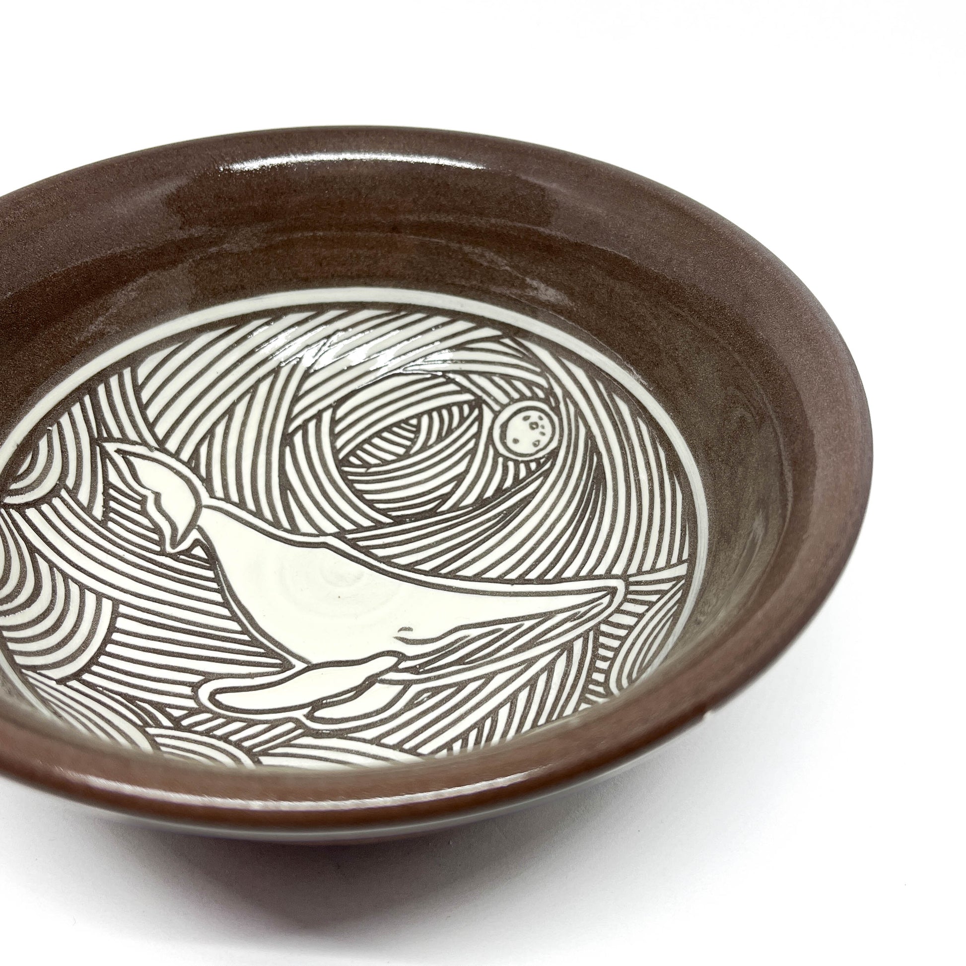 Side view of a bowl interior with a carved dolphin leaping through stylized waves.