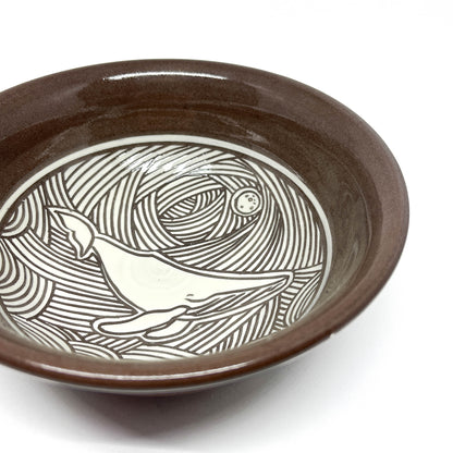 Side view of a bowl interior with a carved dolphin leaping through stylized waves.