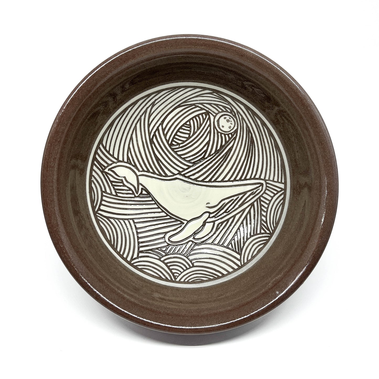 Overhead view of a ceramic bowl with a detailed dolphin carving in a wave-filled seascape.