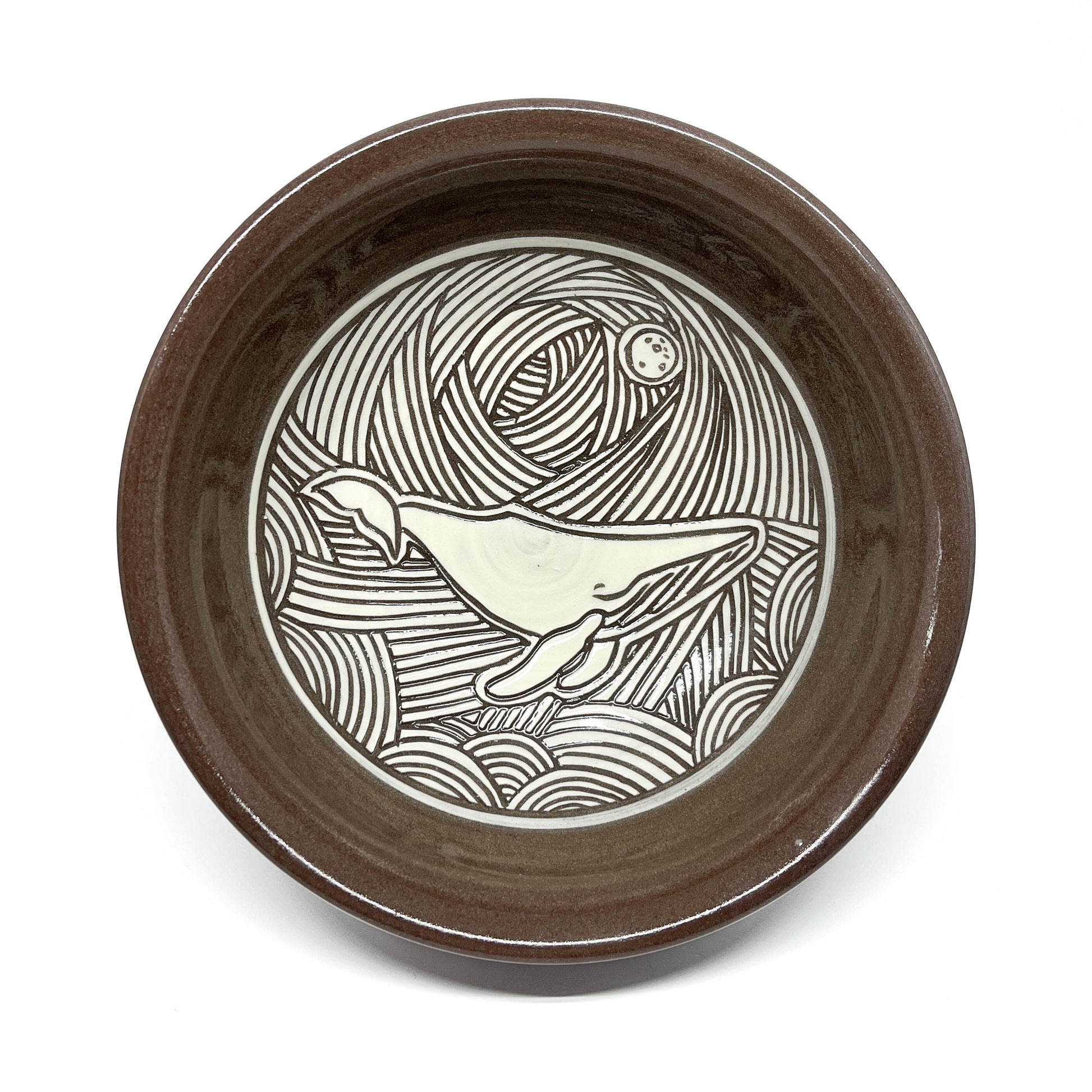 Overhead view of a ceramic bowl with a detailed dolphin carving in a wave-filled seascape.