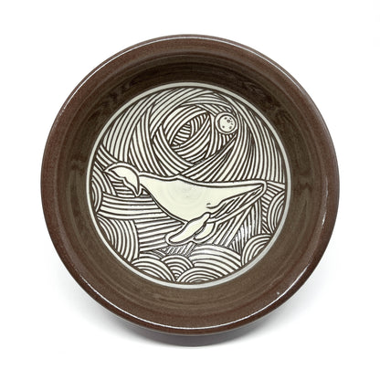 Overhead view of a ceramic bowl with a detailed dolphin carving in a wave-filled seascape.