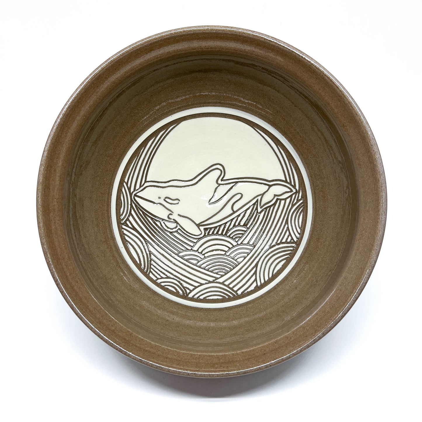 Bowl with carved sperm whale swimming in front of a large circular sun above textured waves.