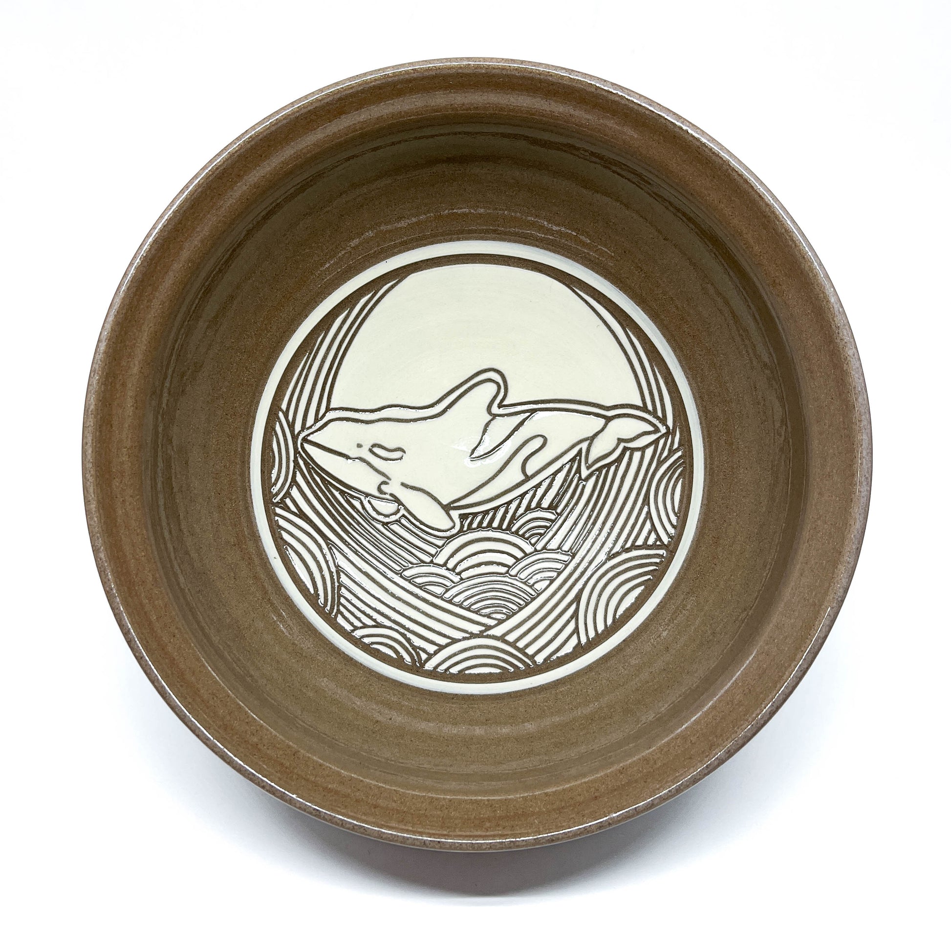 Bowl with carved sperm whale swimming in front of a large circular sun above textured waves.