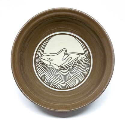 Bowl with carved sperm whale swimming in front of a large circular sun above textured waves.
