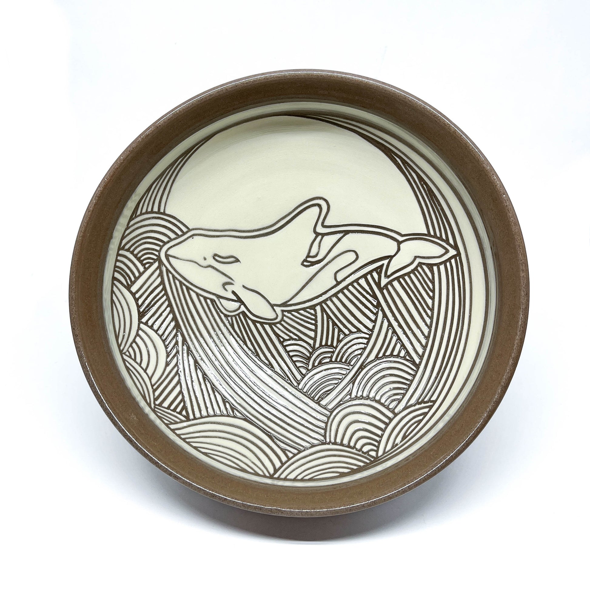 Underside of a ceramic bowl showing unglazed foot with carved wave motif on the base.