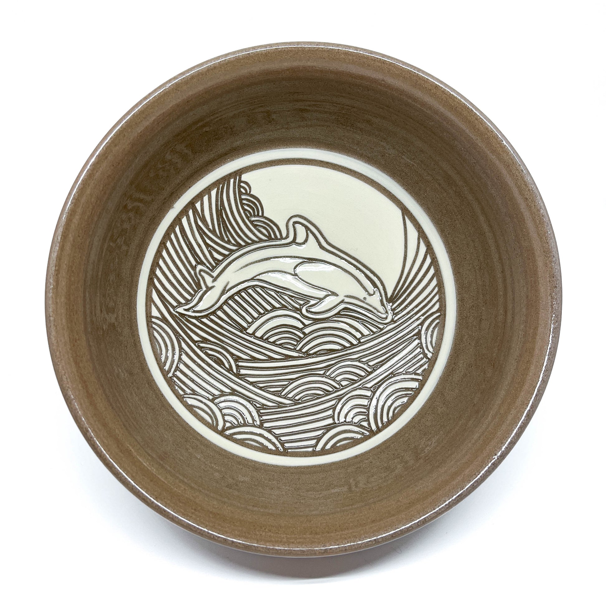 Top-down view of a bowl with whale carving and detailed wave background, moon visible above.