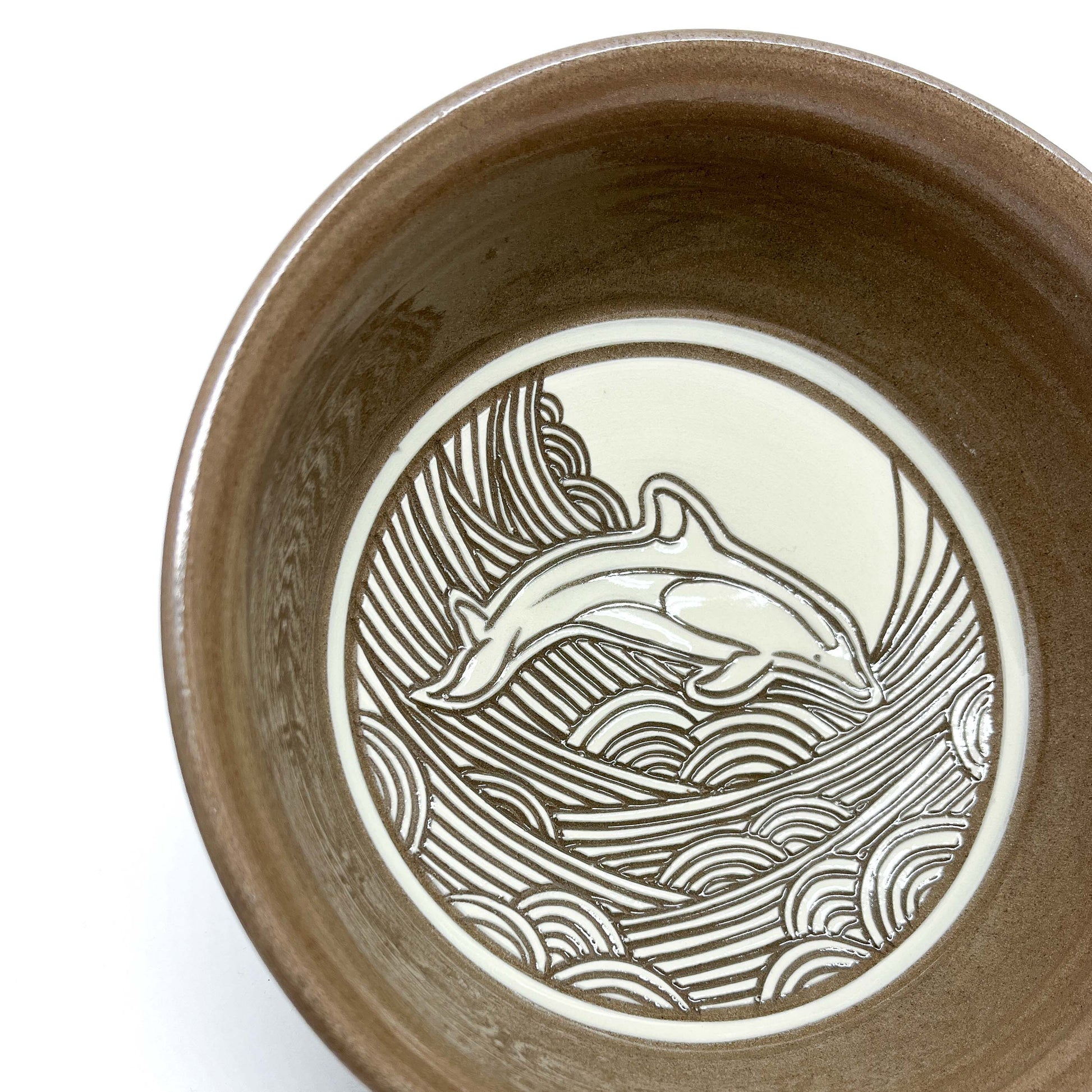 Angled close-up of a ceramic bowl featuring a whale and moon set in a swirling ocean pattern.