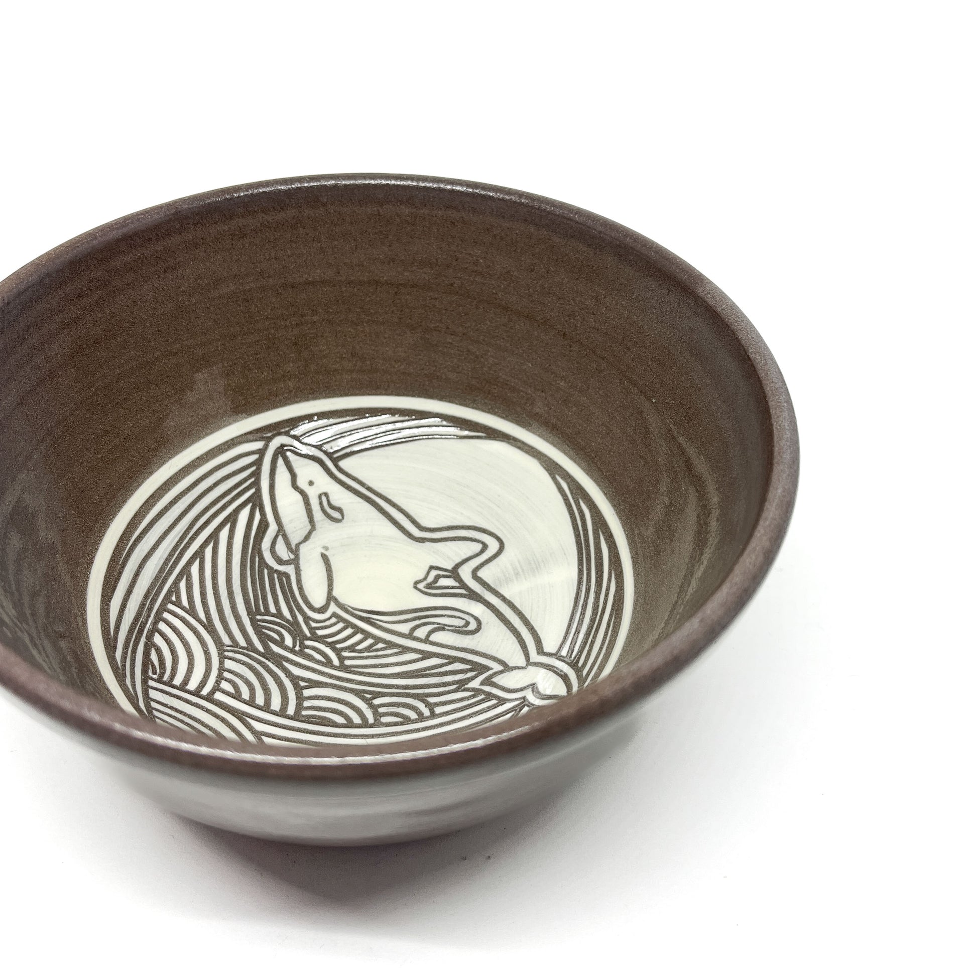 Close-up of a ceramic bowl with an etched orca whale design surrounded by flowing waves.