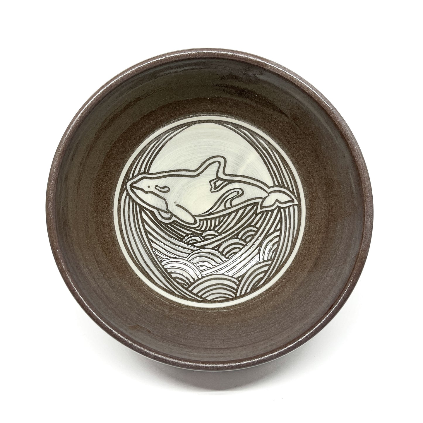 Top-down view of a ceramic bowl featuring a circular whale motif surrounded by stylized waves.