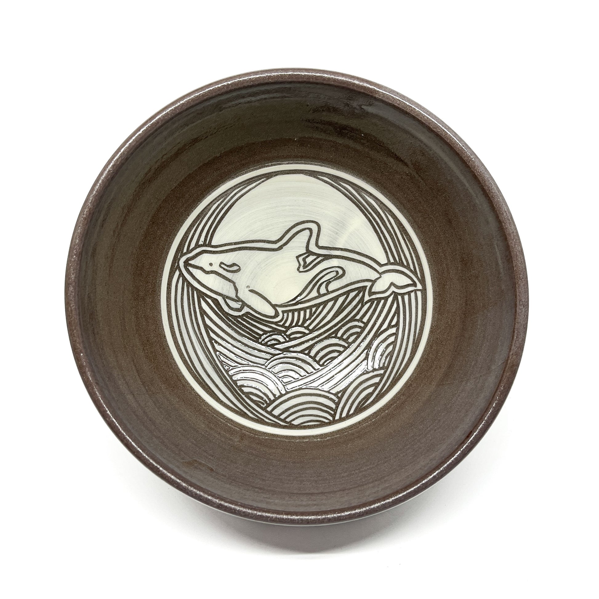 Top-down view of a ceramic bowl featuring a circular whale motif surrounded by stylized waves.