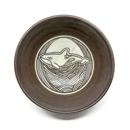 Top-down view of a ceramic bowl featuring a circular whale motif surrounded by stylized waves.