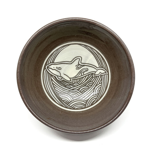 Top-down view of a ceramic bowl featuring a circular whale motif surrounded by stylized waves.