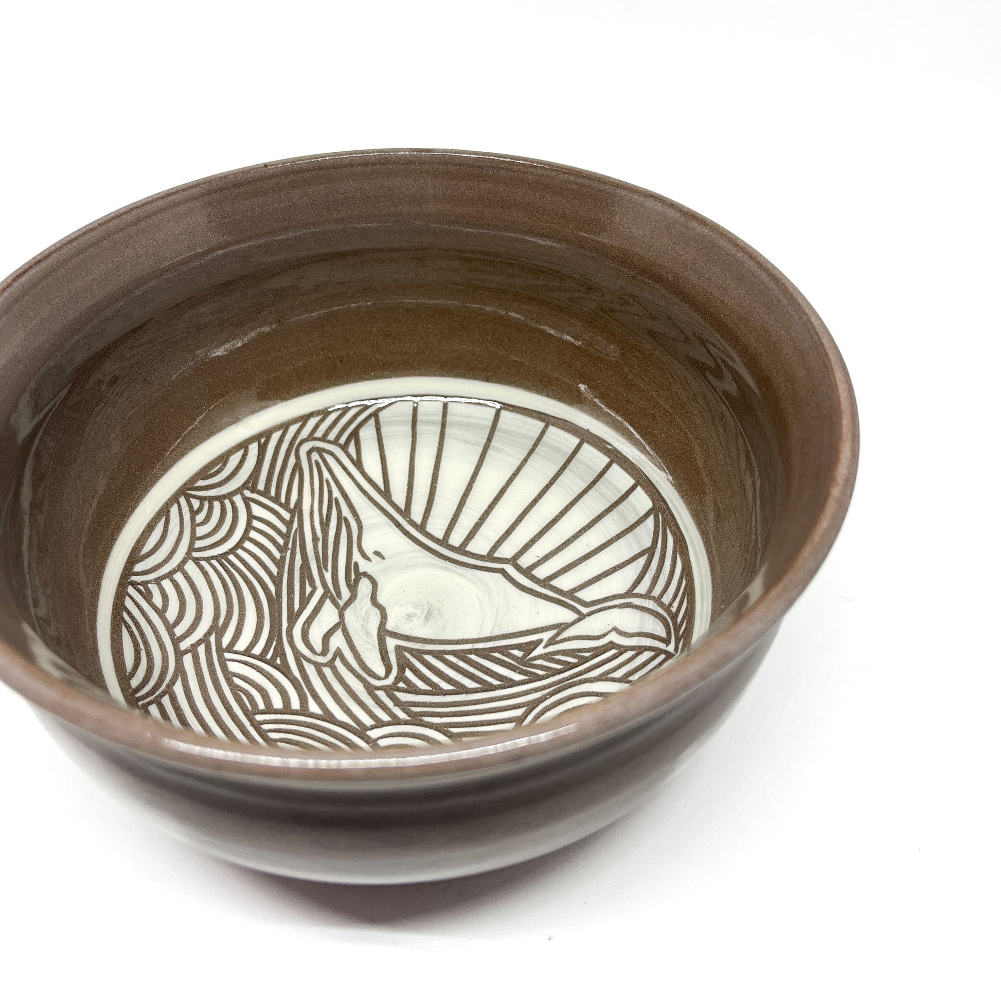 Angled view of a ceramic bowl featuring an etched whale design with stylized waves and radiating lines inside.