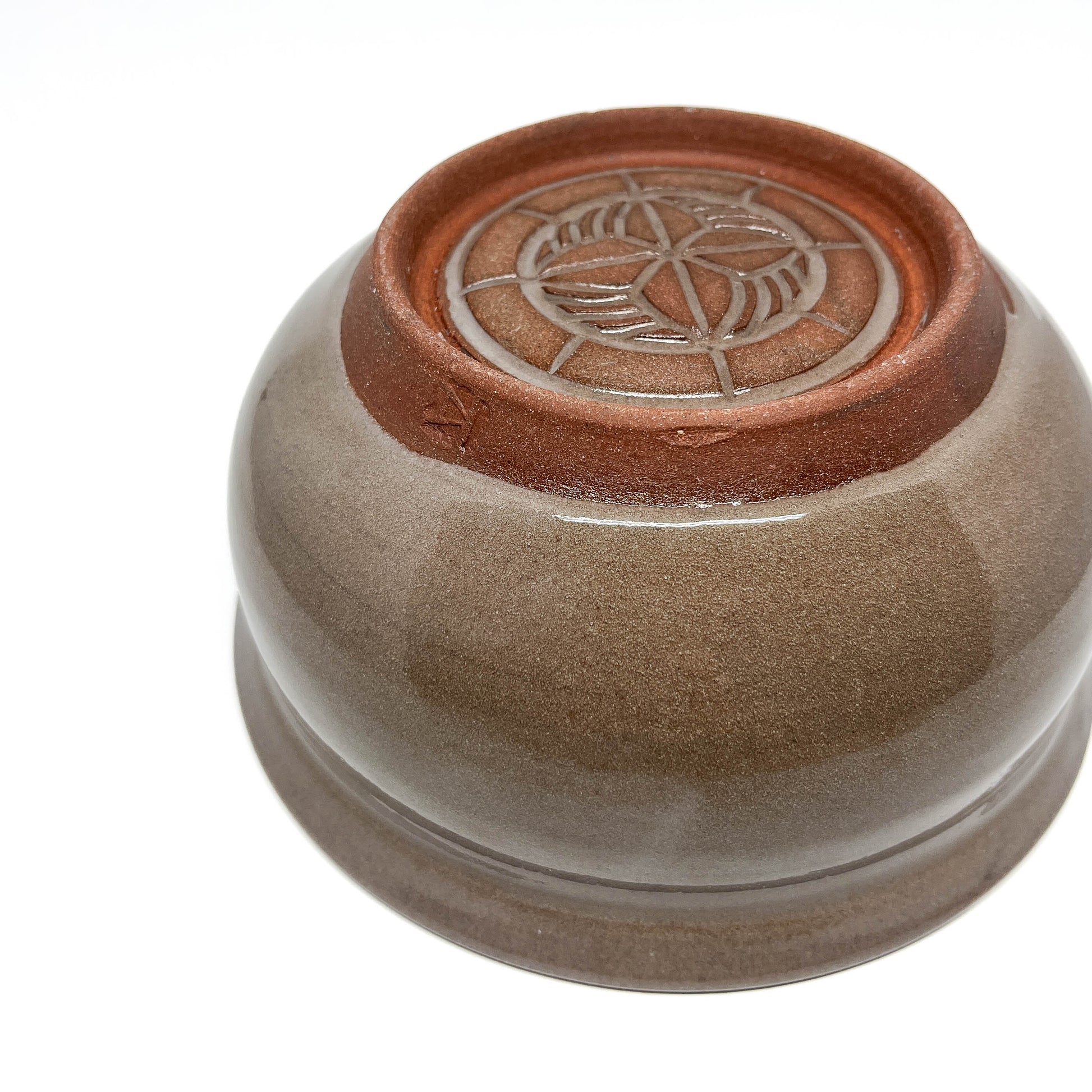 Bottom view of a ceramic bowl showing a carved circular pattern and maker’s mark on the unglazed foot.