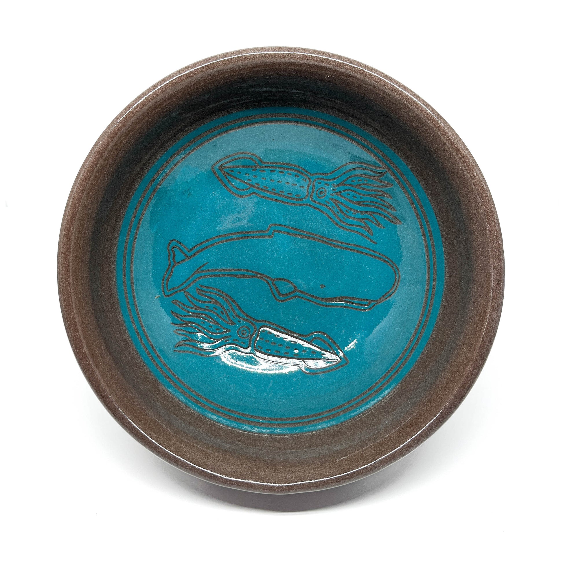 Ceramic bowl featuring etched designs of a whale surrounded by two squid in a circular underwater scene.