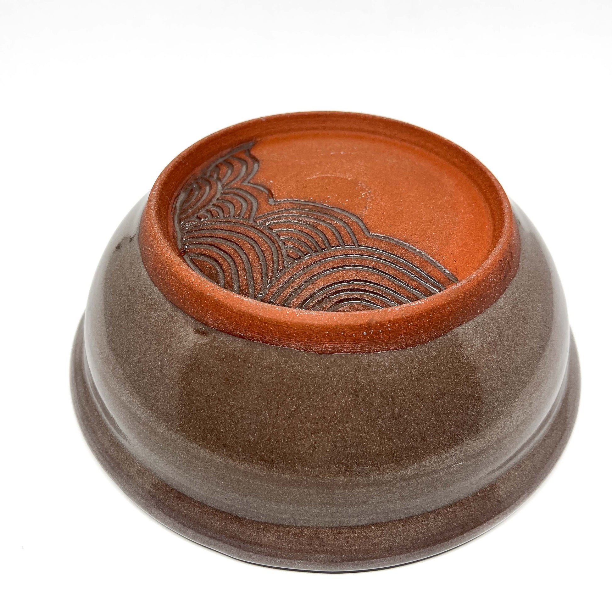 Bottom view of a ceramic bowl featuring a carved wave pattern on the unglazed foot.