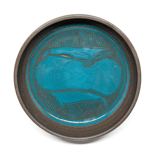 A teal ceramic bowl with an engraved pattern sits on four feet.