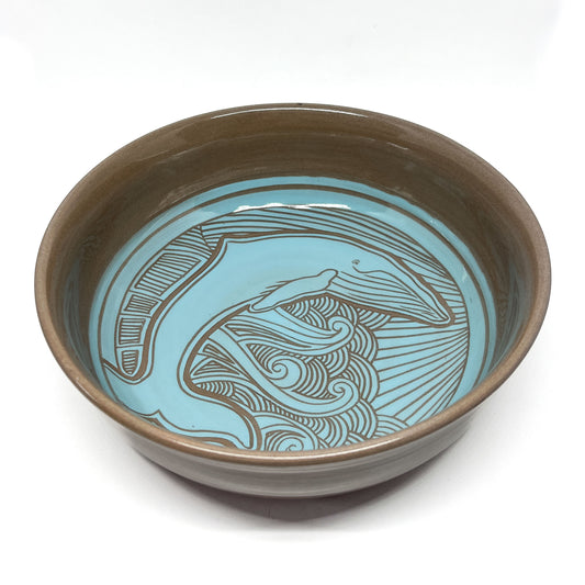 Ceramic bowl featuring a carved humpback whale design surrounded by swirling lines and radiant beams.