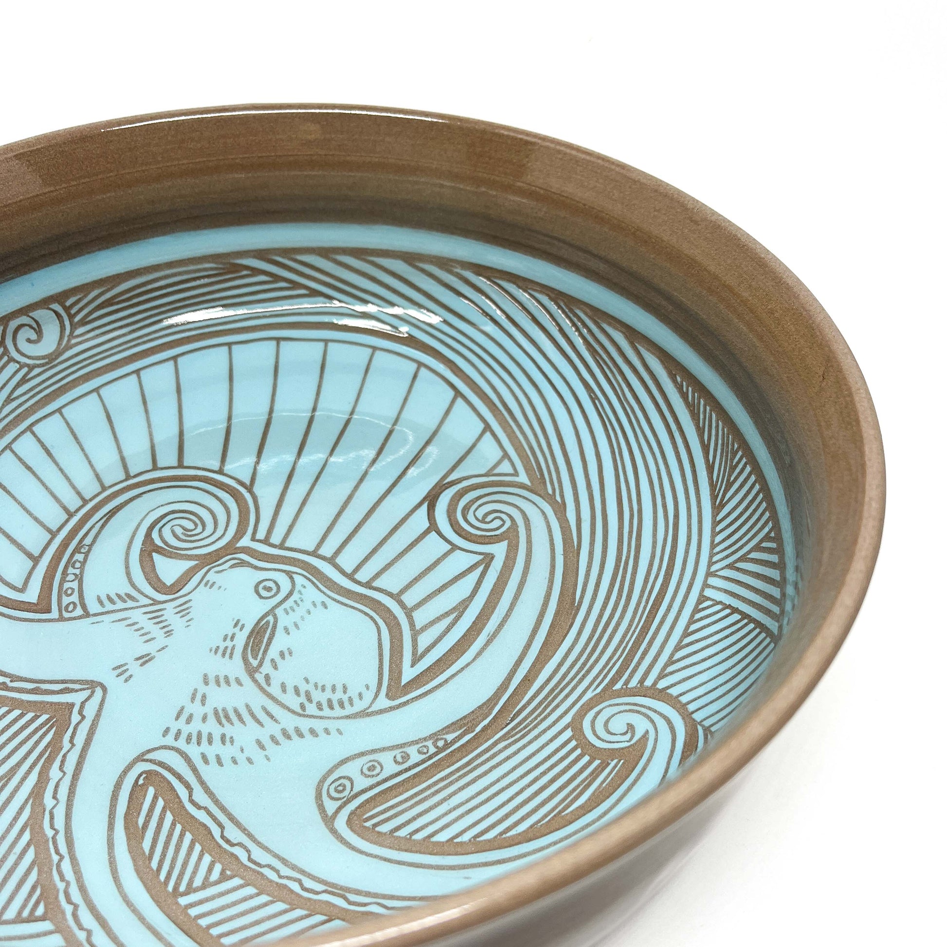 Angled close-up of a bowl interior with a carved humpback whale, spiraling waves, and radiating lines.
