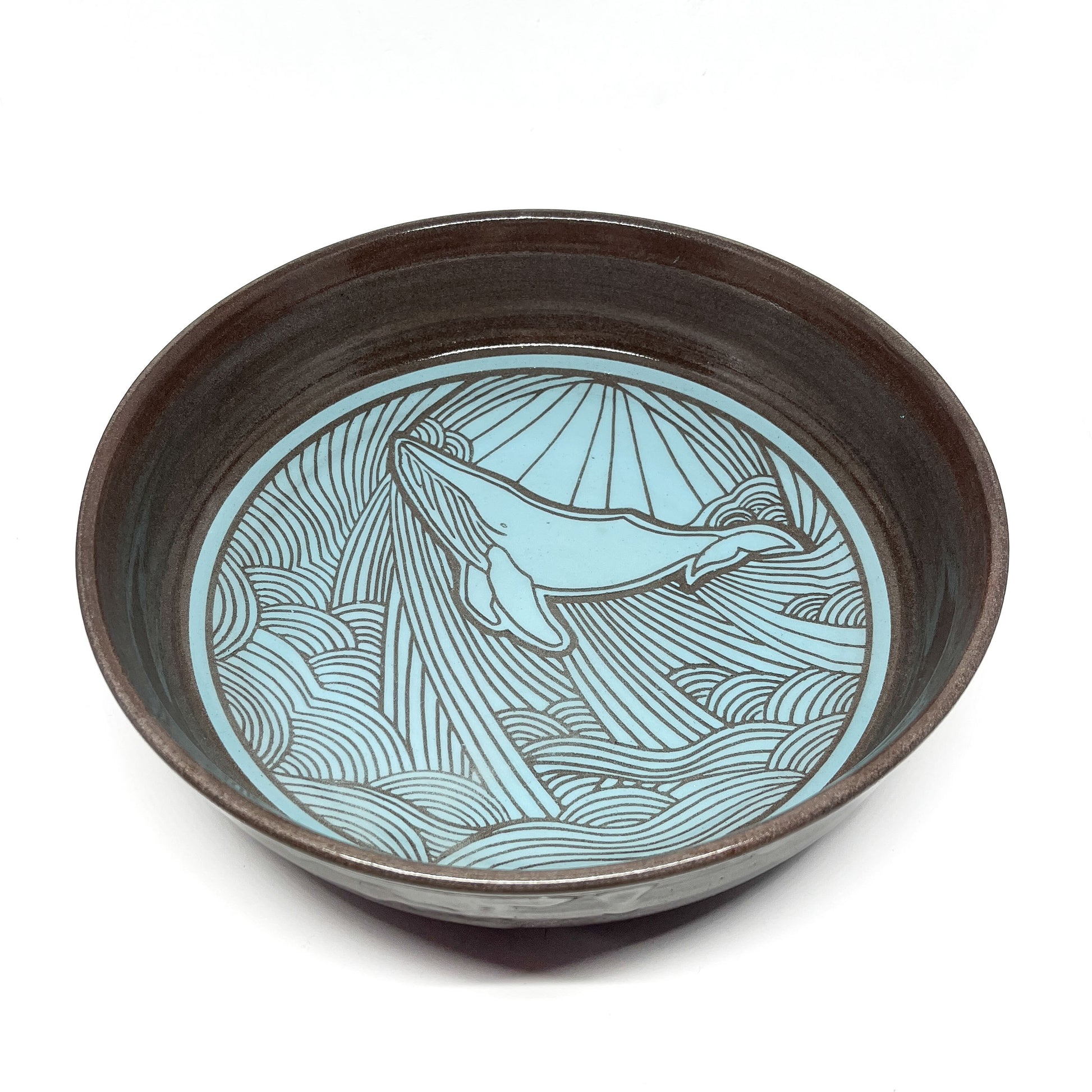 Angled top view of a bowl with a whale swimming through stylized waves and rays in the background.