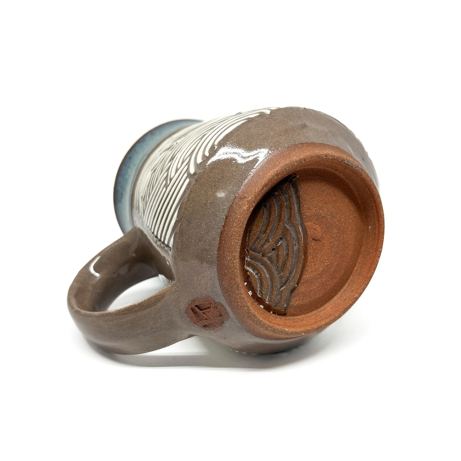 Bottom of handmade ceramic mug showing unglazed base with wave texture and maker’s mark.