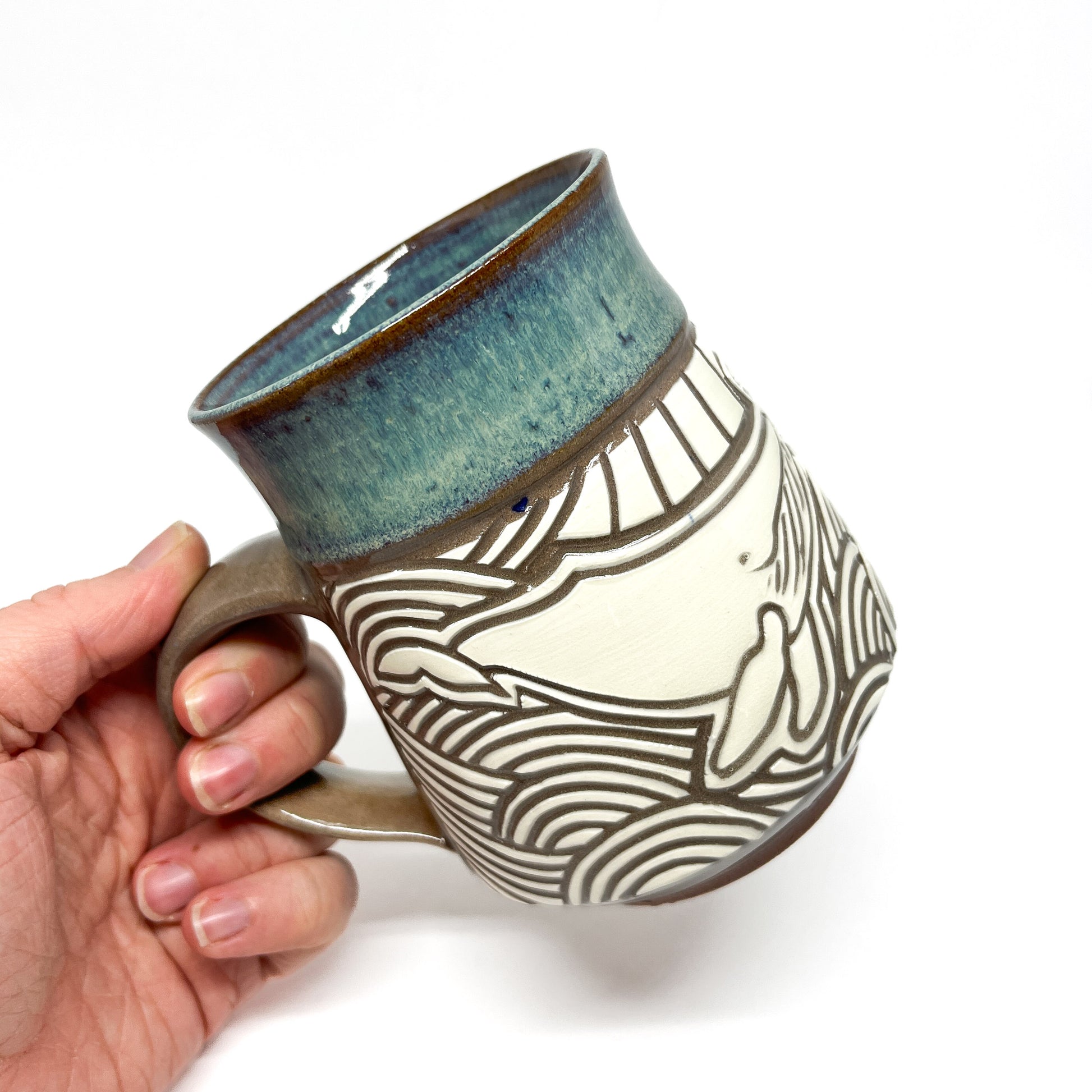 Side view of ceramic mug showing two carved whales facing each other above stylized ocean waves.