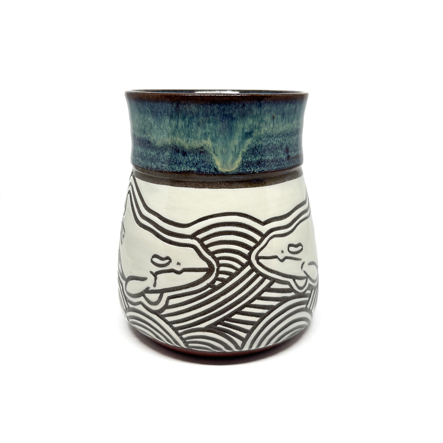 Ceramic mug held in hand, highlighting a carved whale motif and glossy, glazed upper section.