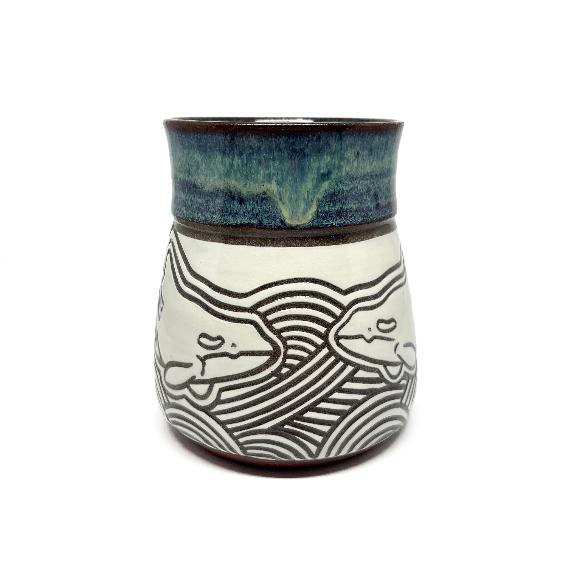 Ceramic mug held in hand, highlighting a carved whale motif and glossy, glazed upper section.