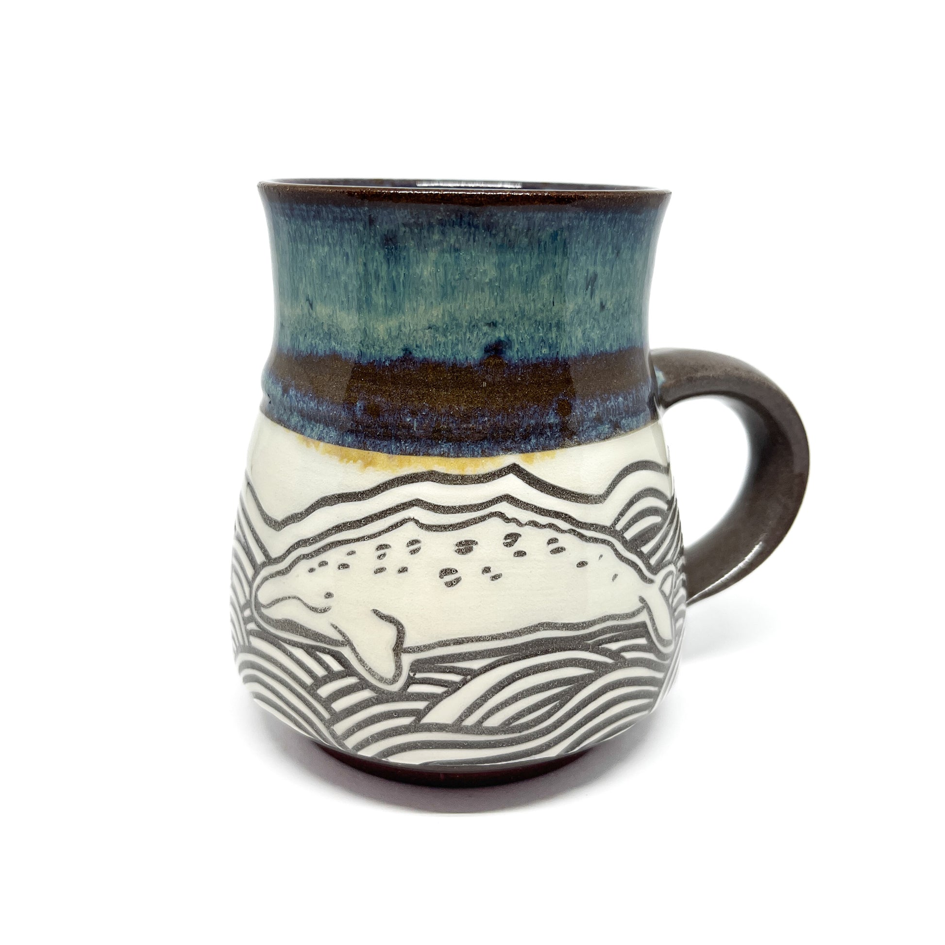 Whale carved into a ceramic mug swimming through stylized waves, topped with a textured glaze.