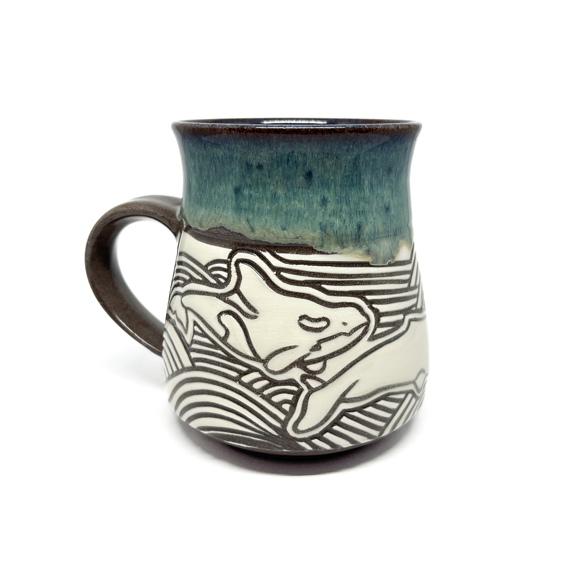 Two carved whales swim in opposite directions across the back of the mug, set above wave patterns.