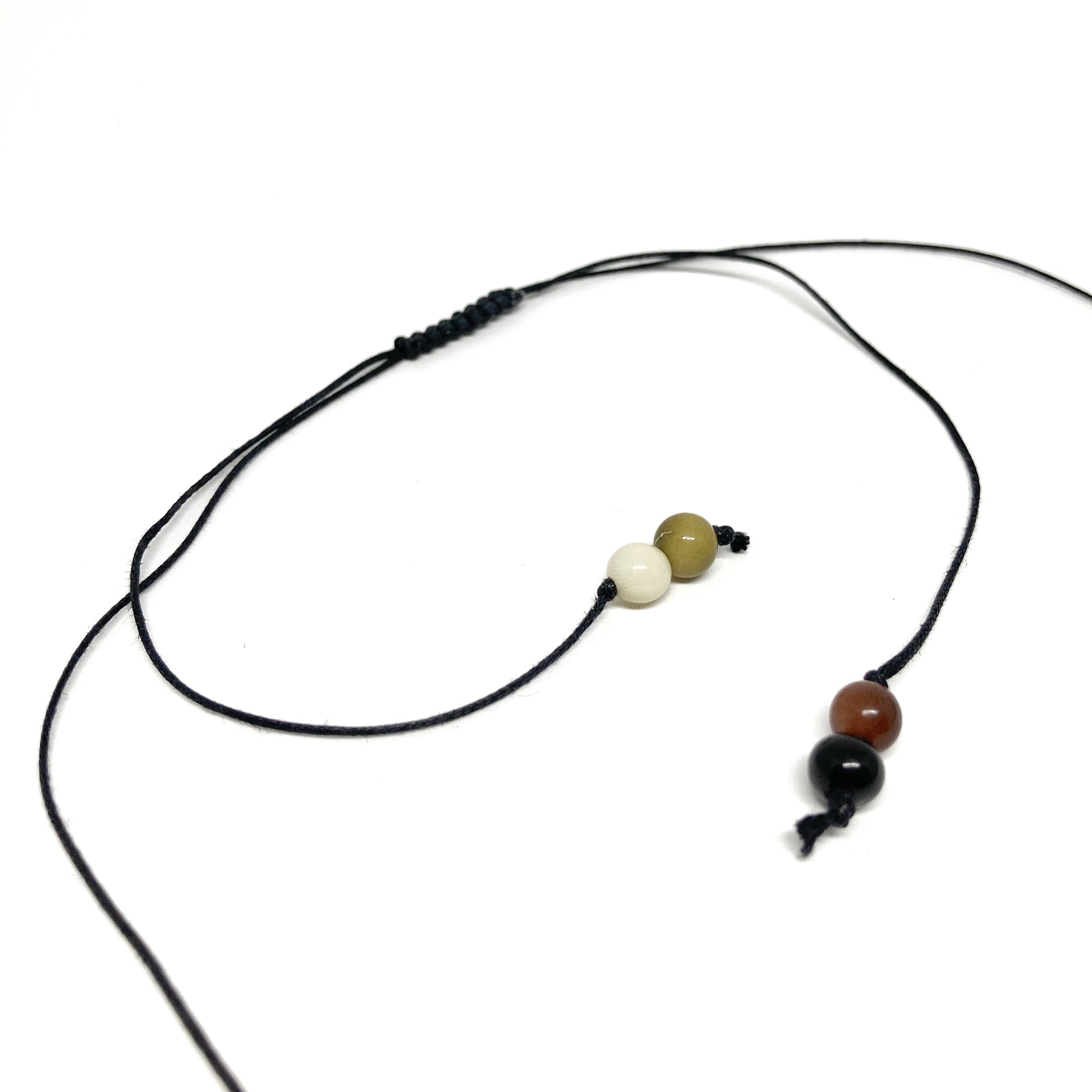 A close-up of a black cord necklace with three small beads in earth tones.