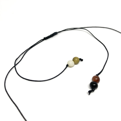 A close-up of a black cord necklace with three small beads in earth tones.