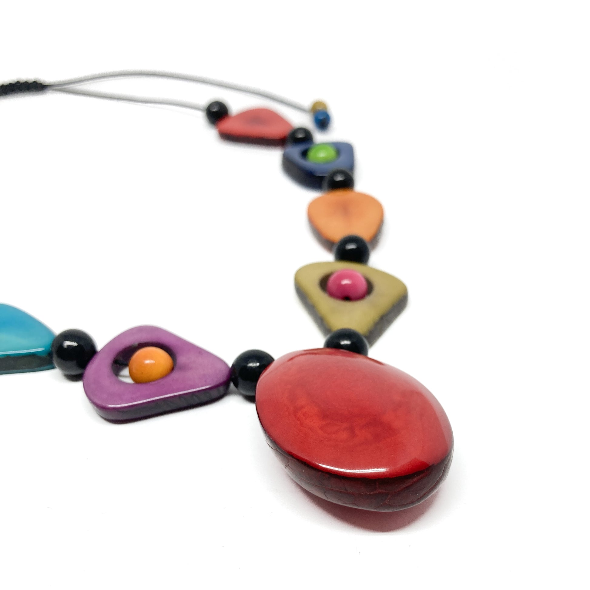 A close-up of a necklace with colorful, irregularly shaped stones and black beads, focusing on the red stone.