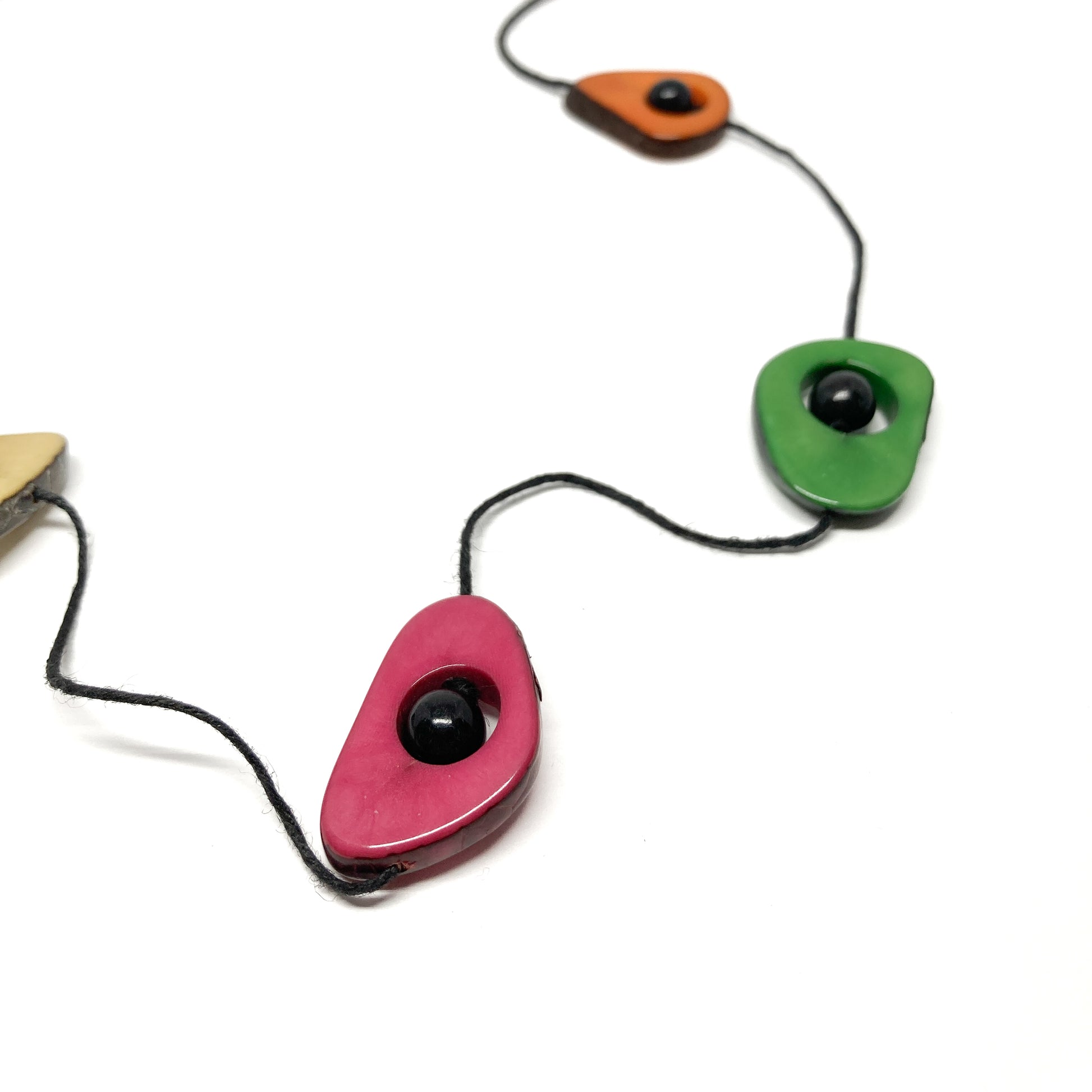 A close-up of a necklace with colorful stones and black beads on a thin black cord, laid flat.