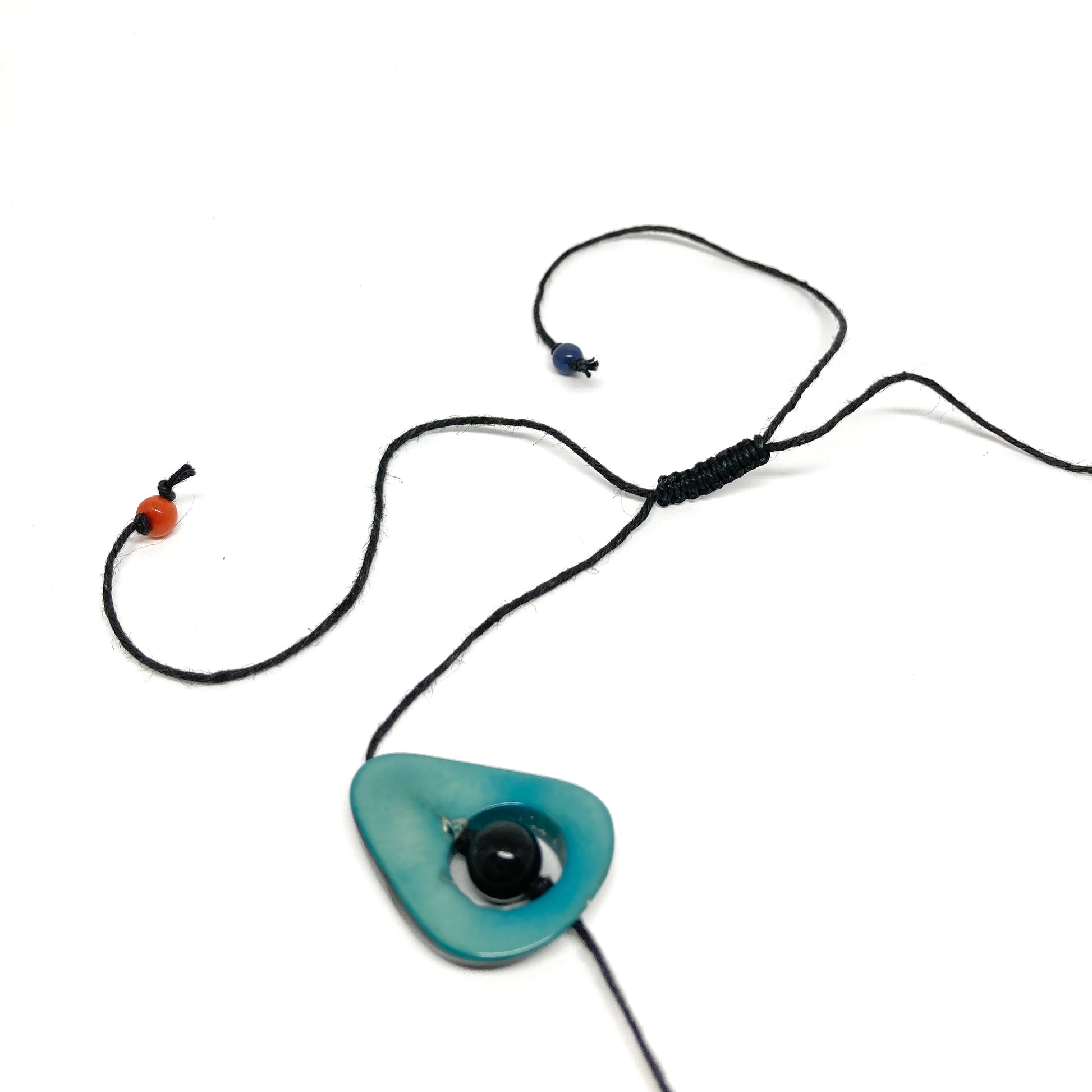 A close-up of a necklace with a blue stone, black bead, and black cord on a white background.
