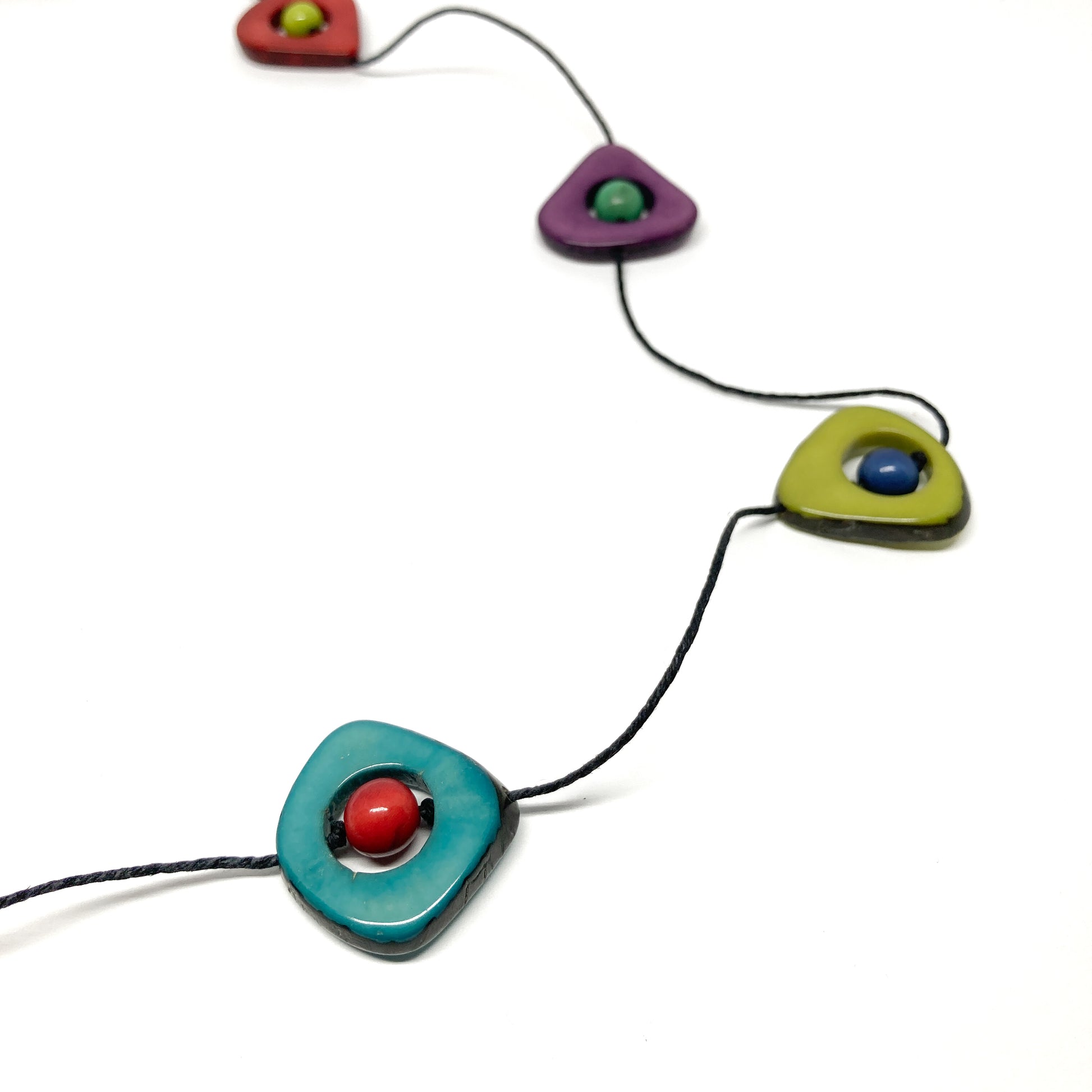A close-up of a necklace with colorful stones and black beads on a thin black cord, laid flat.