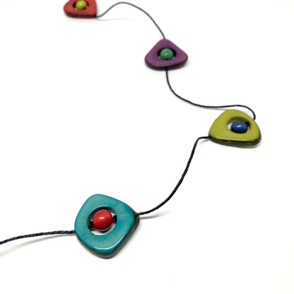 A close-up of a necklace with colorful stones and black beads on a thin black cord, laid flat.