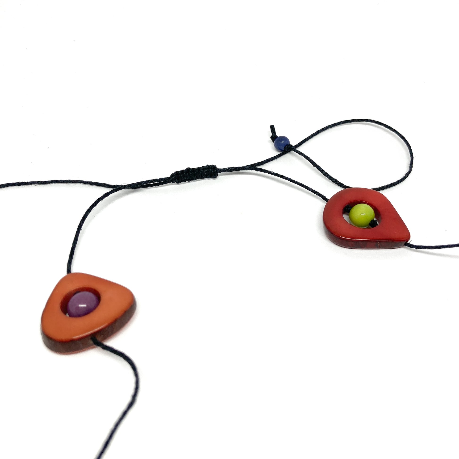 A close-up of a necklace with colorful stones and black beads on a thin black cord, laid flat.