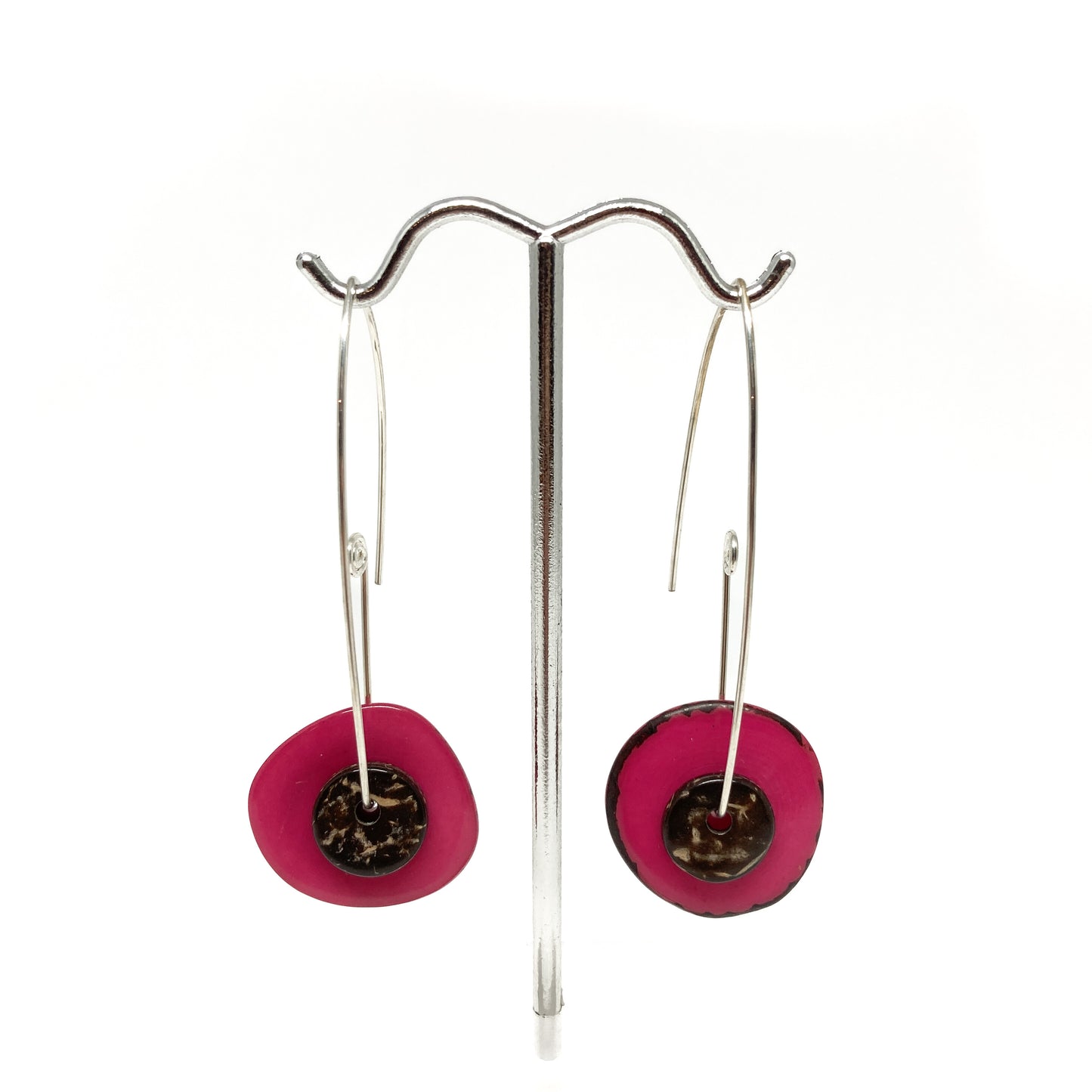 Two pink earrings with silver pins and round metal details on a stand.