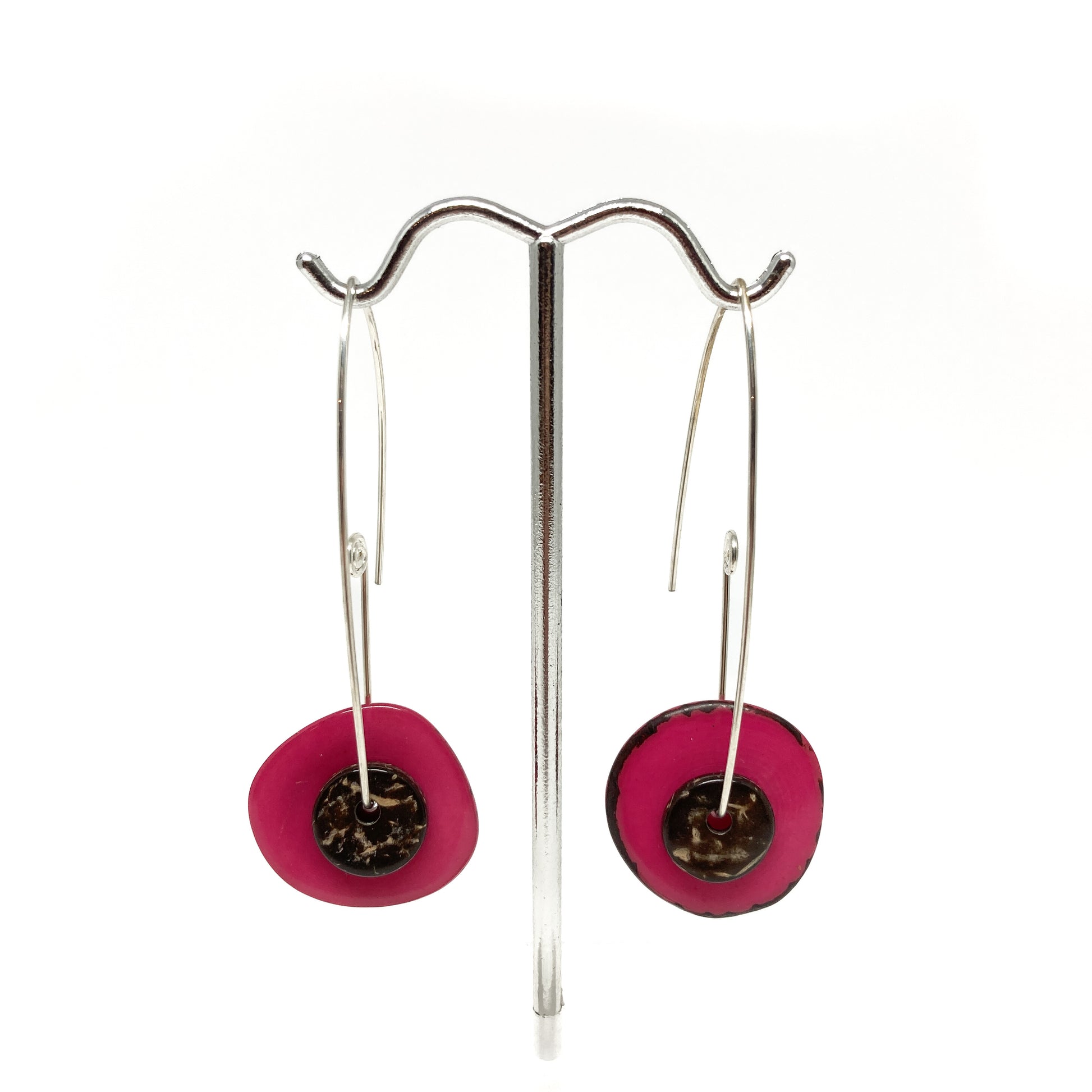 Two pink earrings with silver pins and round metal details on a stand.