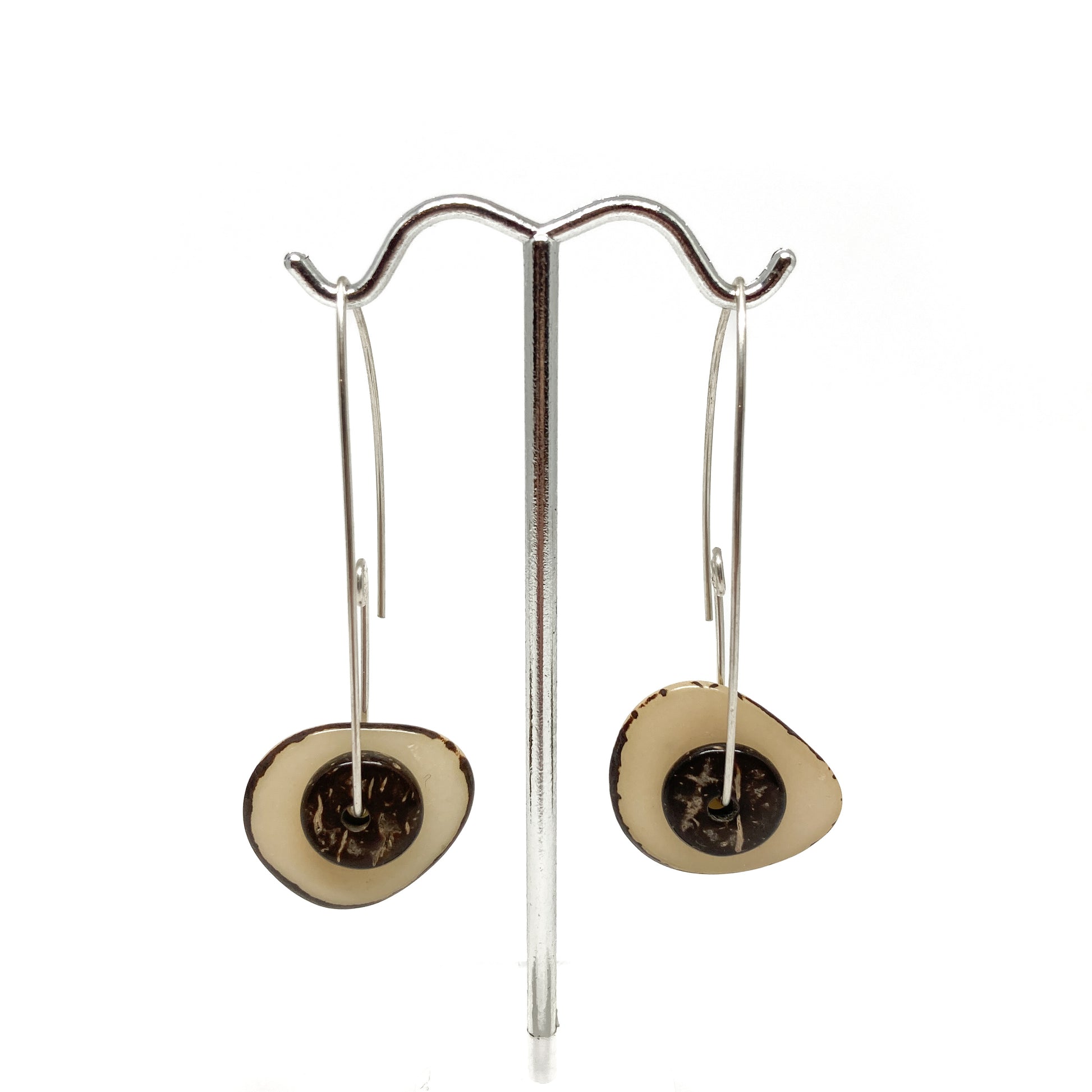 Two beige earrings with silver pins and round metal details on a stand.