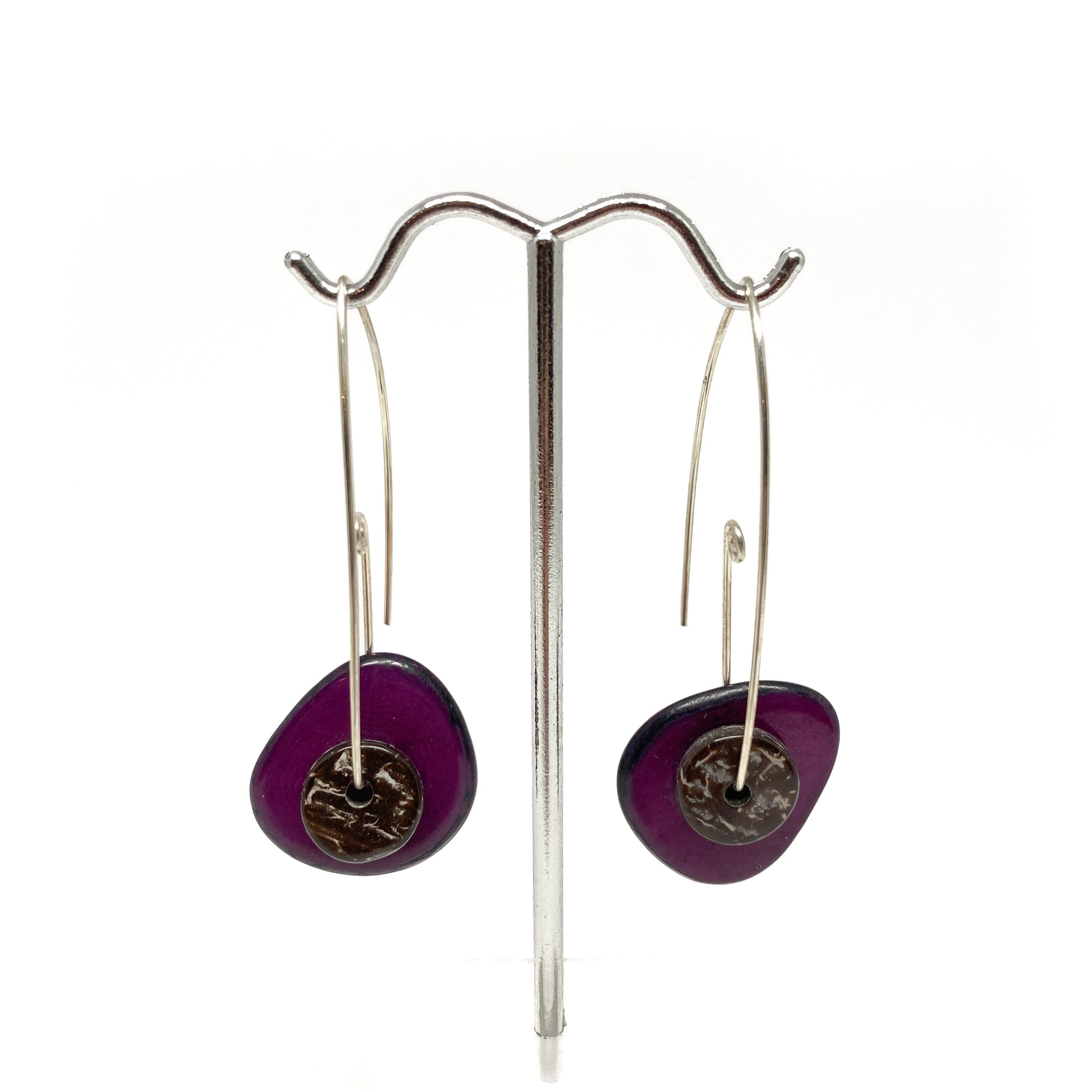 Two purple earrings with silver pins and round metal details on a stand against a white background.
