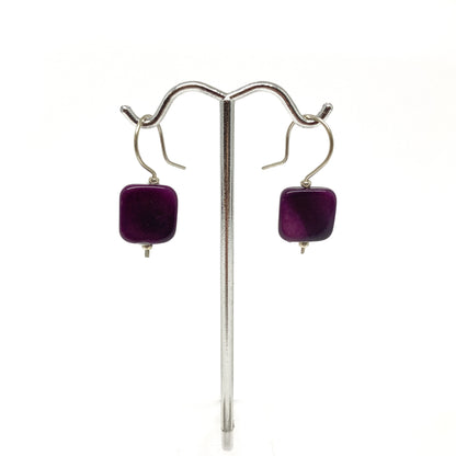 Two purple square earrings with silver hooks on a stand.