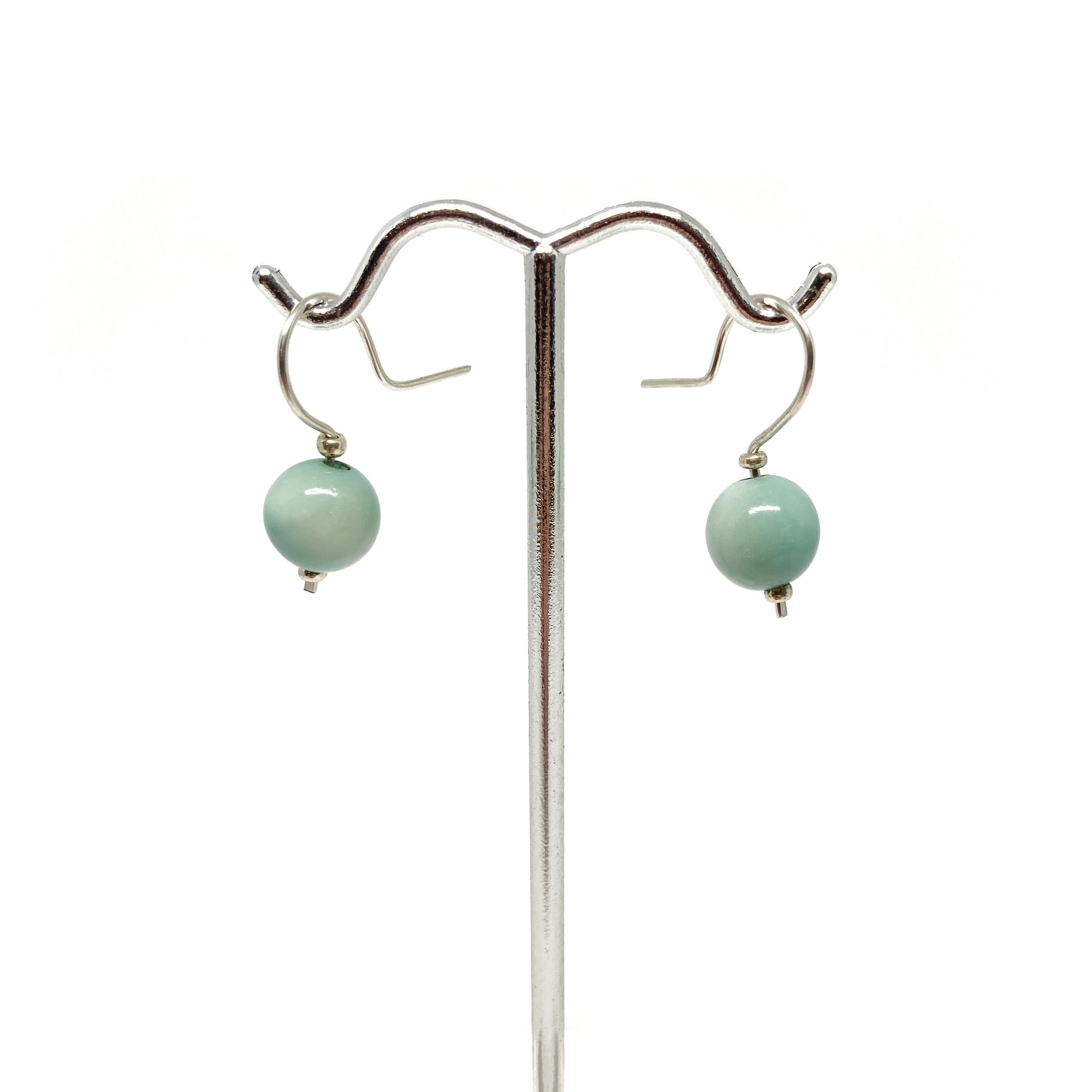 Two light blue pearl earrings with silver hooks on a stand.